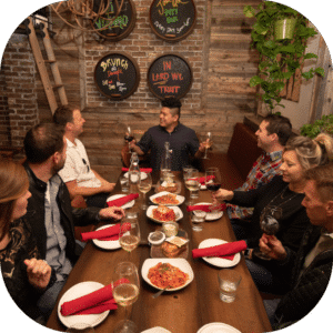 Group sitting at table with a tour guide holding wine glasses in Little Italy, San Diego