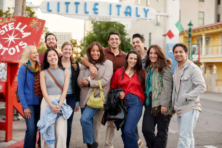 tour group of ten people posing in front of blue little italy sign