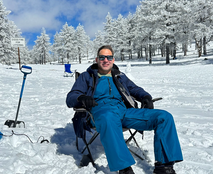 man sitting in chair surrounded by snow and trees