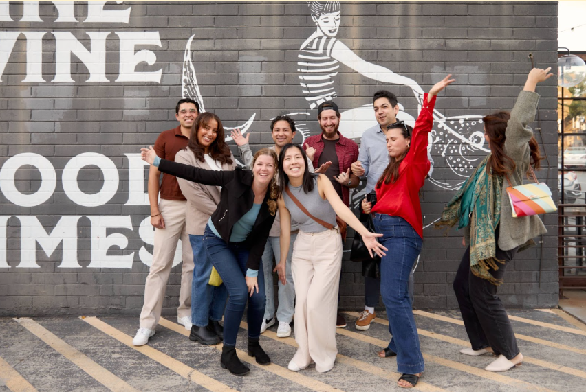 group of people standing posing in front of grey brick wall